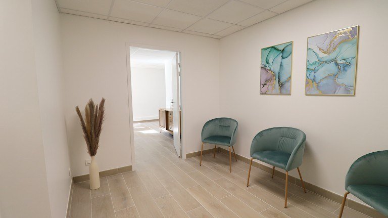 Salle d’accueil avec fauteuils en velours vert et tableaux.