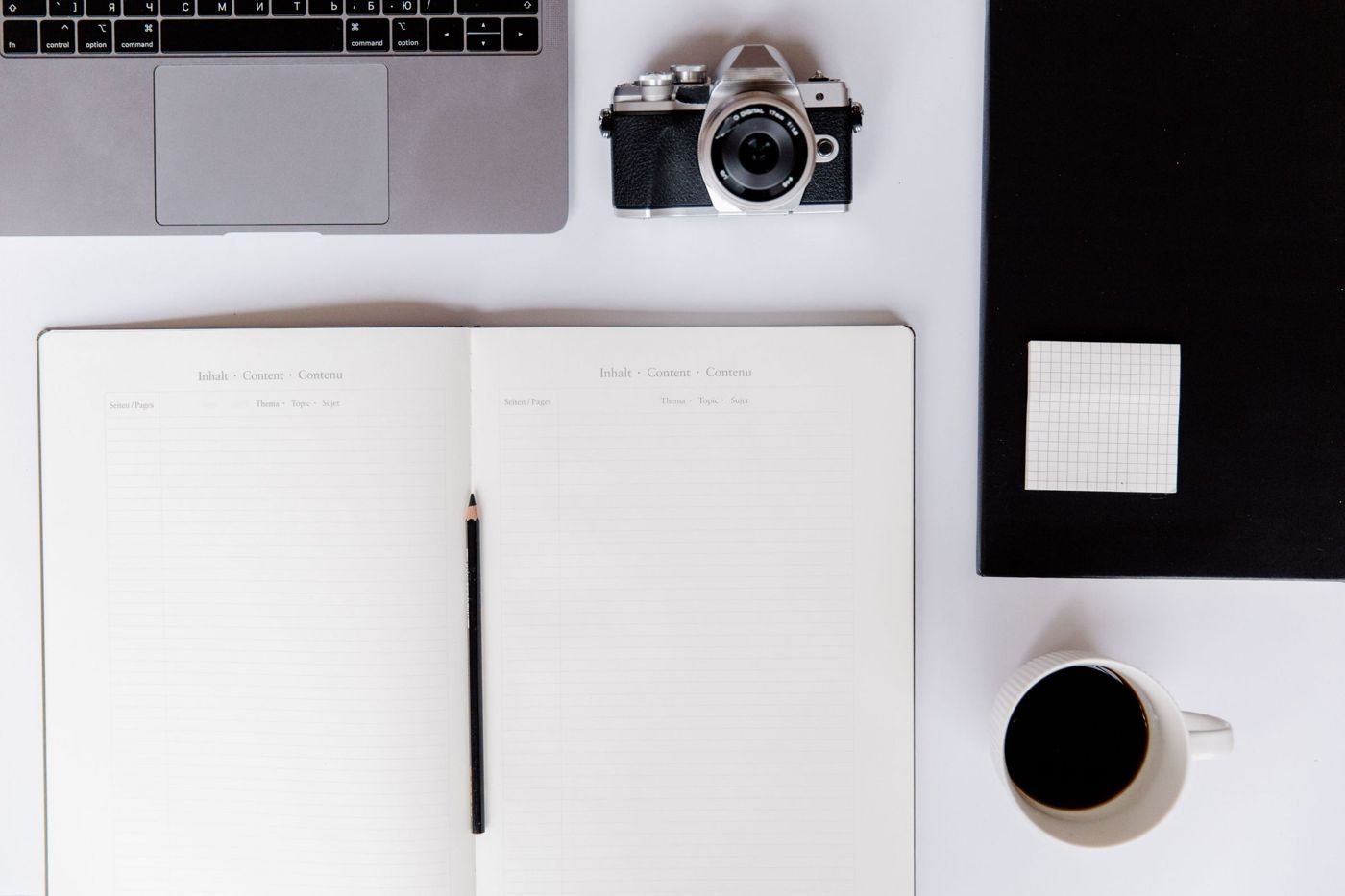 Carnet ouvert, ordinateur, appareil photo et café sur un bureau clair.